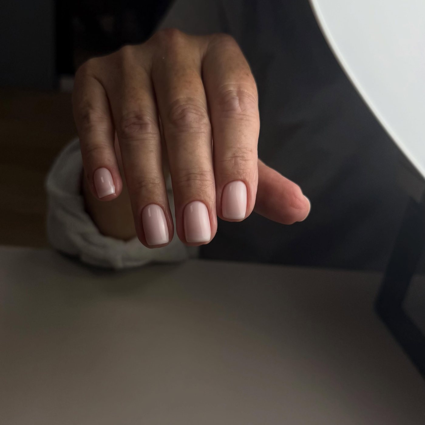 Hand met lichtroze, glanzende nagels naast een witte doek