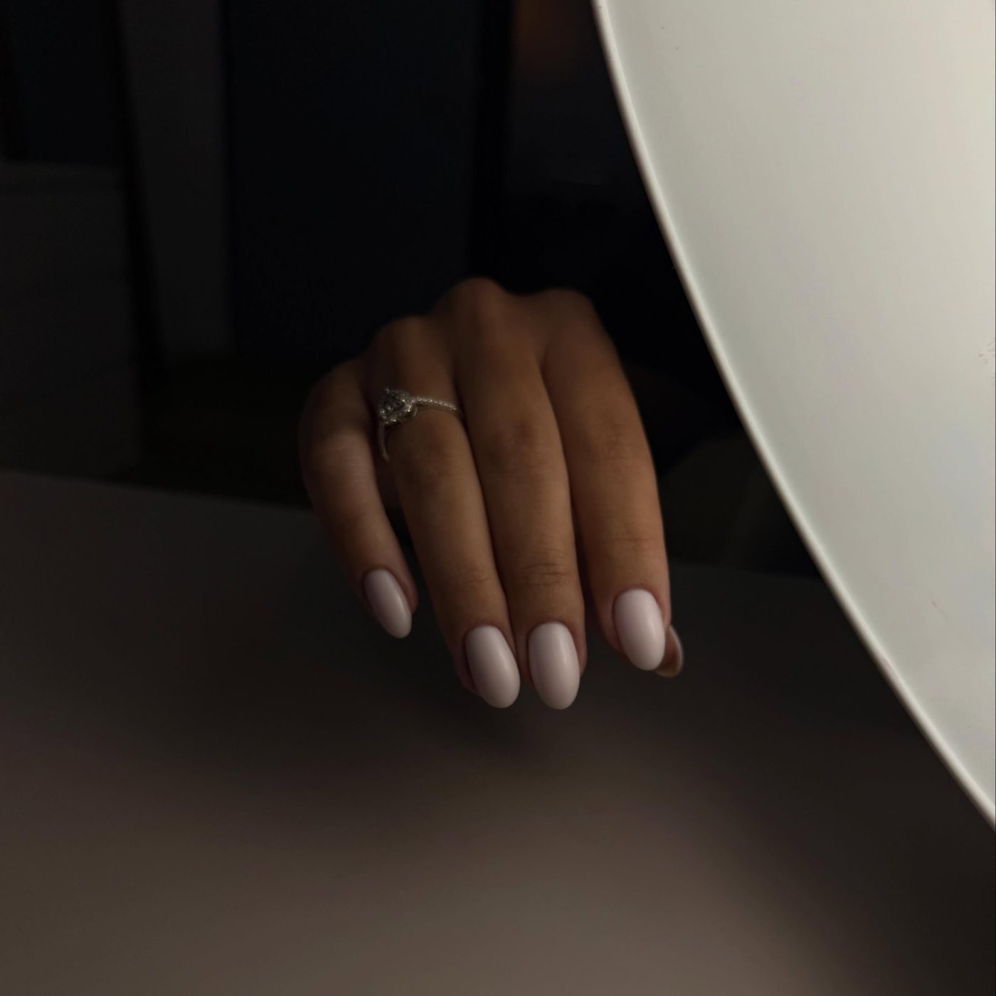Hand met een ring en melkwitte, ovale nagels