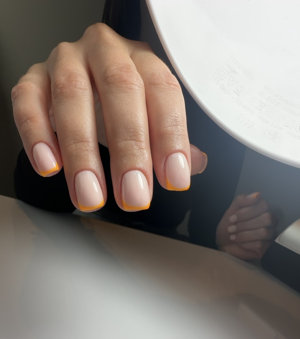 Hand met korte, vierkante naturel nagels met oranje French tips